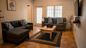 A living room with a sectional sofa, a smaller sofa, a coffee table, and a TV mounted on the wall.