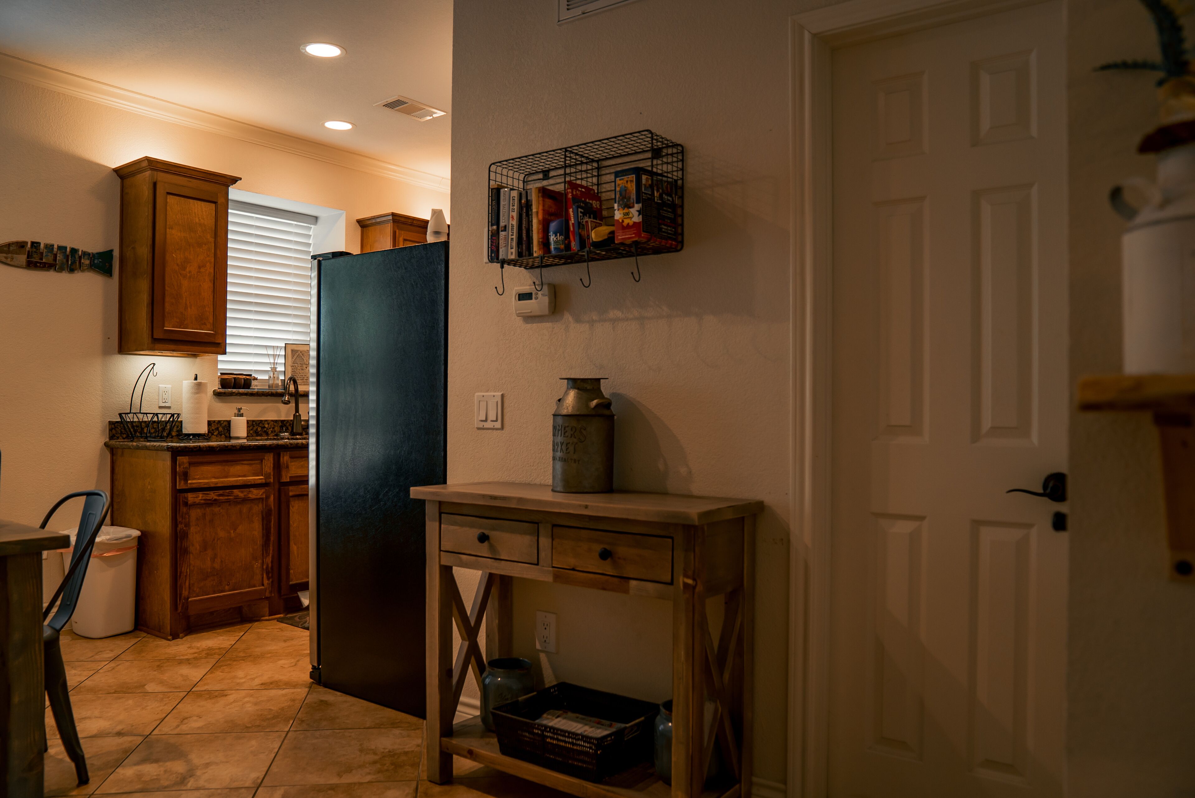A kitchen with wooden cabinets, a black refrigerator, a small table, and a wall-mounted book rack.