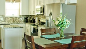 A modern kitchen with white cabinets, a central island, and a dining area with wooden chairs and a table. - 295 is 5 minutes from dam with boat launch and tritoon boat for rent. (Jasper)