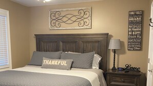 A bedroom with a wooden bed, a ceiling fan, a bedside table with a lamp, a rug, and a wall with family rules. - 295 is 5 minutes from dam with boat launch and tritoon boat for rent. (Jasper)