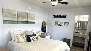 A bedroom with a bed, a ceiling fan, and a wall with a 'Coastal Living' sign.