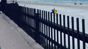 A beach with a wooden fence, a concrete walkway, and the ocean in the background.