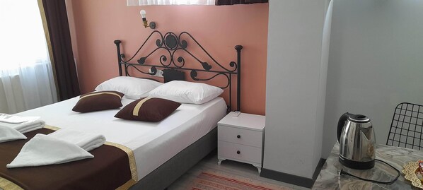 Cama bem arrumada com travesseiros, mesa de cabeceira com chaleira e criado-mudo.