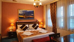 A hotel room with a bed, bedside lamps, a star-shaped ceiling light, a painting of a lighthouse, a dining table, and a red chair. - Emirhan Hotel - Adults Only (Istanbul)