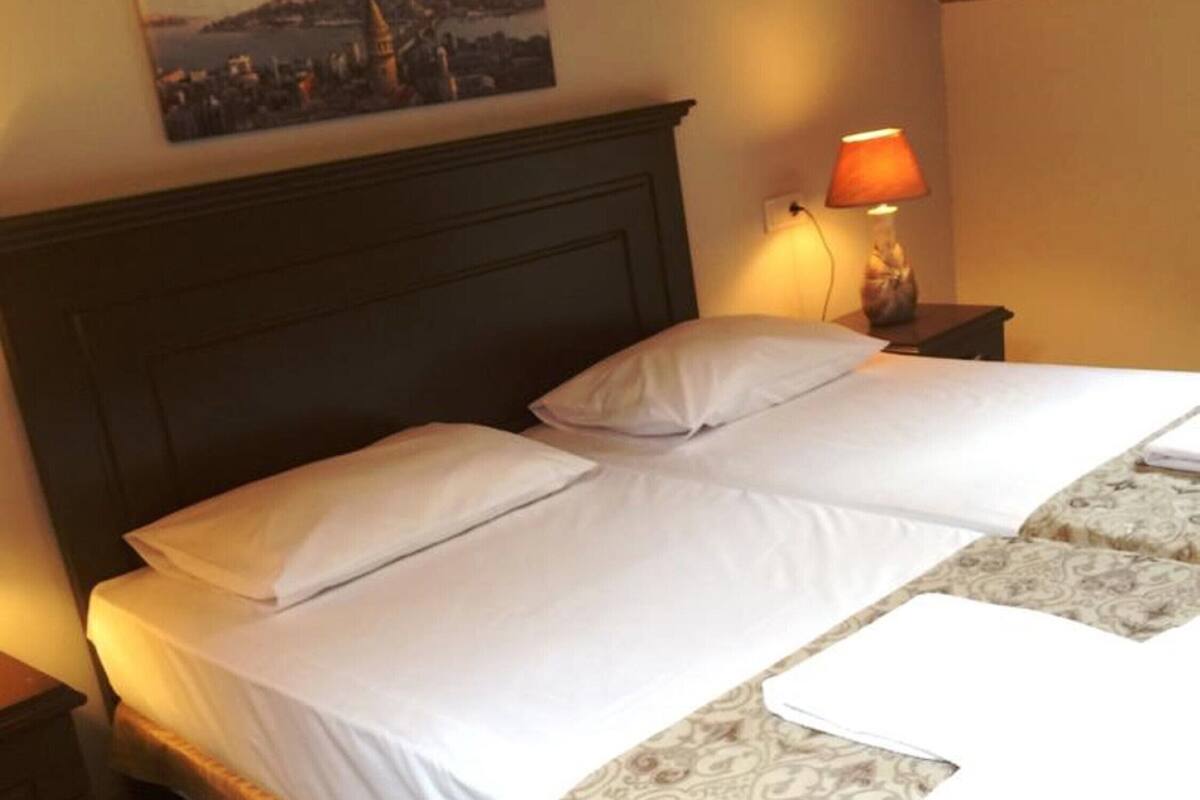 A hotel room with a bed, a nightstand, a lamp, and an air conditioner.