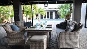 A covered outdoor seating area with wicker furniture and a pool in the background. - Esmeralda Escape - Your Private Oasis (Noord)