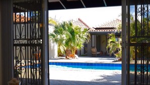A swimming pool with a tiled deck, surrounded by palm trees and a building with a tiled roof. - Esmeralda Escape - Your Private Oasis (Noord)