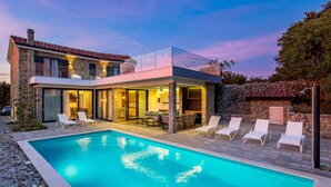 Een modern huis met een zwembad, terras en stenen muren.