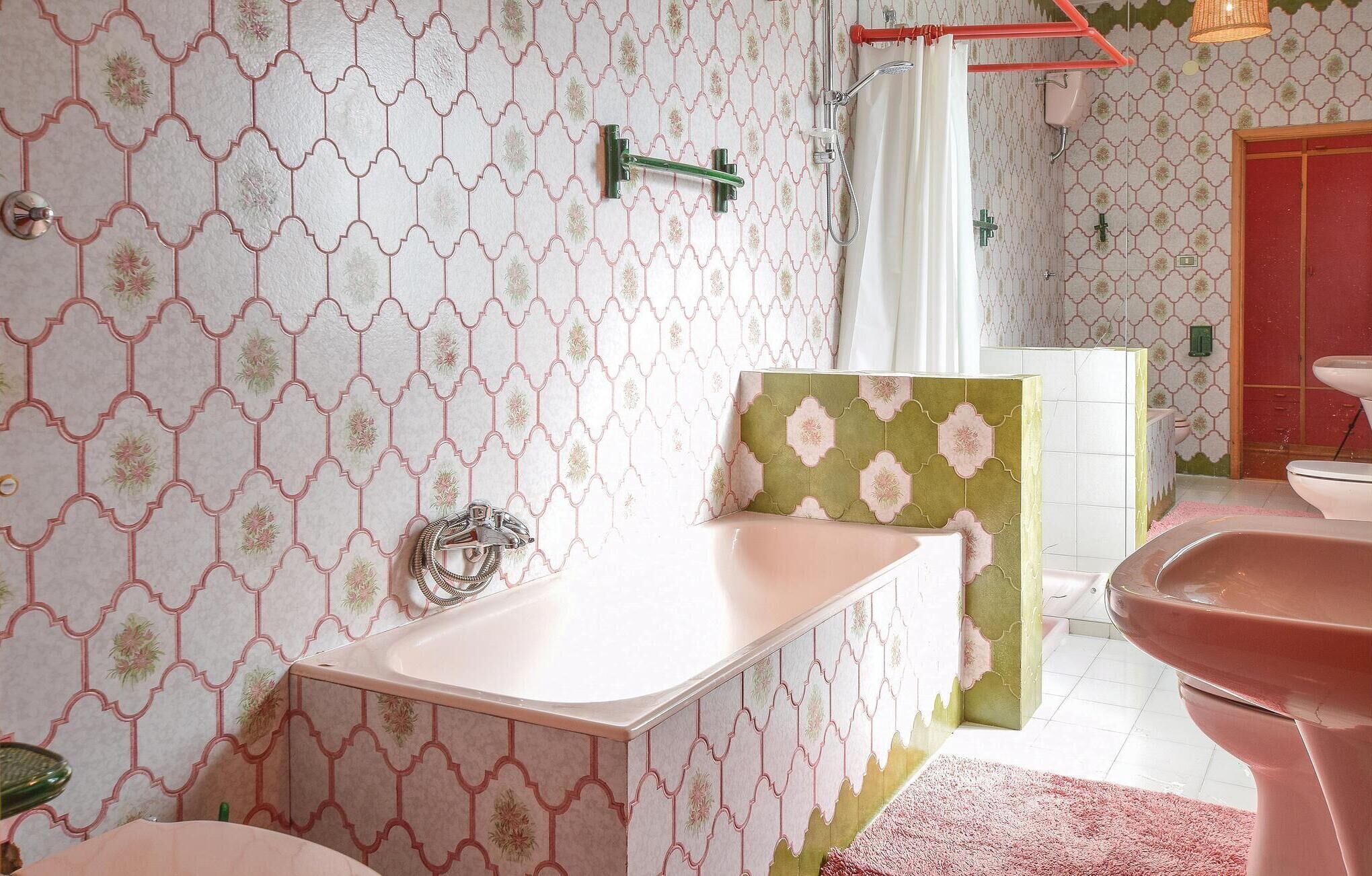 A bathroom with patterned wallpaper, a bathtub, a shower, and a toilet.
