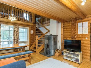 Puinen mökki, jonka sisätiloissa on ruokailutila, takka, televisio ja portaikko.