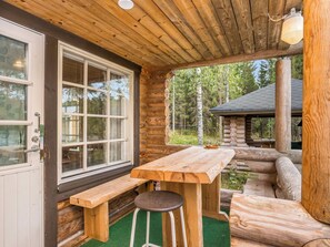 A log cabin with a wooden table and bench, a window, and a view of the surrounding forest.