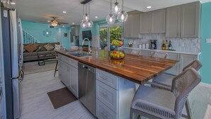 A modern kitchen with a central island, stainless steel appliances, and a dining area with wicker chairs. - WOW! 3 BR! Remodeled waterfront unit, Sapphire Beach, ocean view, private patio (St Thomas)