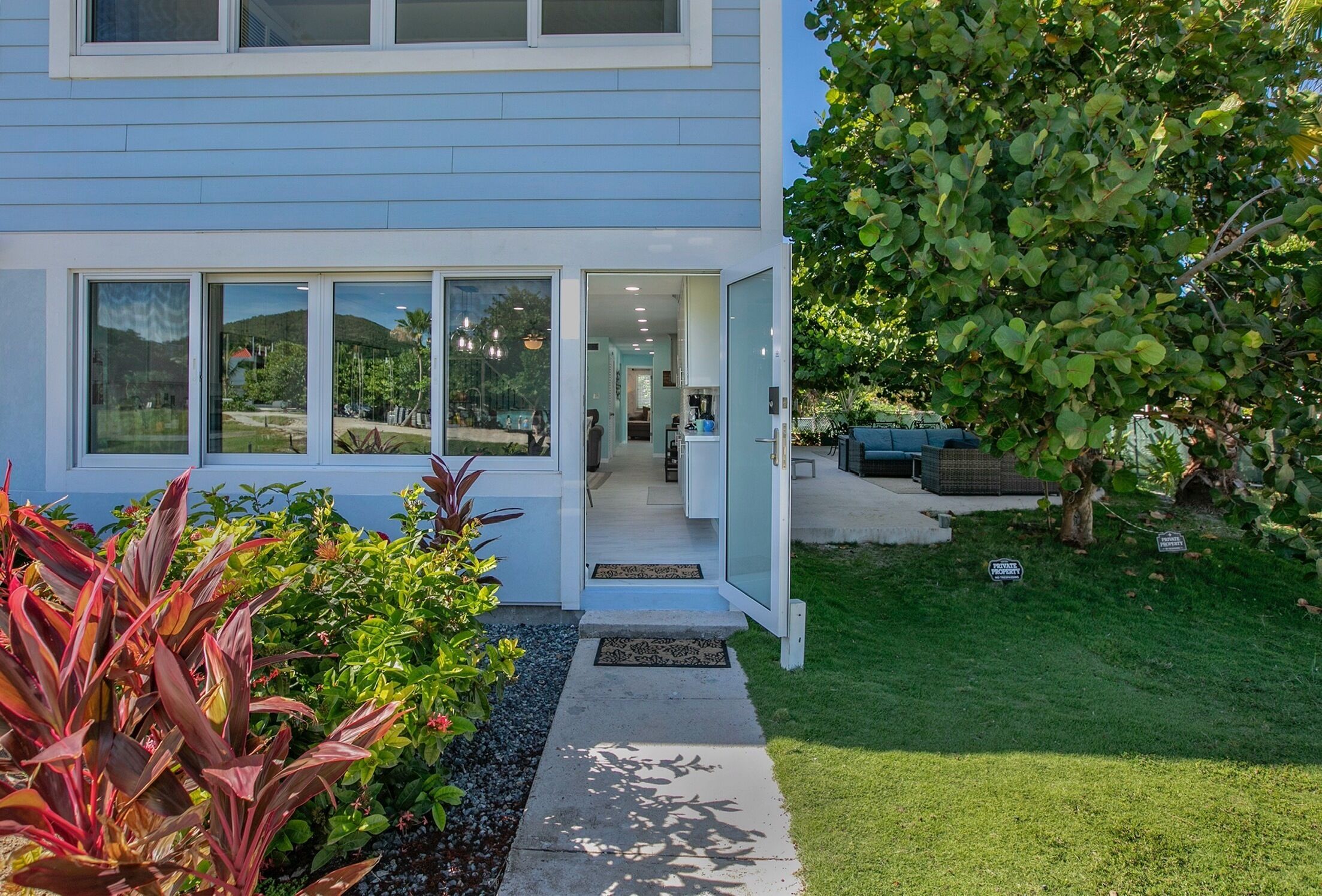 A modern two-story house with large windows, a visible kitchen, and a well-maintained garden.