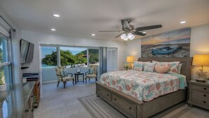 A bedroom with a large bed, a ceiling fan, a TV, and a view of the outdoors. - WOW! 3 BR! Remodeled waterfront unit, Sapphire Beach, ocean view, private patio (St Thomas)