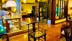 A spacious living area with a wooden floor, a glass partition, and a dining table with chairs. - Pousada Terra Do Mar (Búzios)