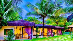A row of thatched-roof cottages with open verandas, surrounded by lush greenery and palm trees. - Pousada Terra Do Mar (Búzios)