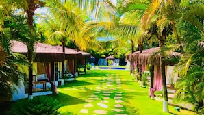 A pathway leading to thatched-roof huts surrounded by lush greenery. - Pousada Terra Do Mar (Búzios)