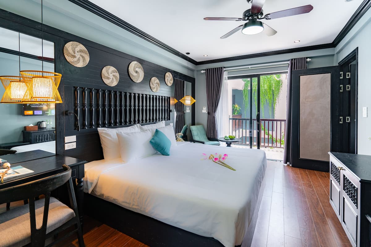 A modern hotel room with a large bed, a desk, and a balcony with a view.