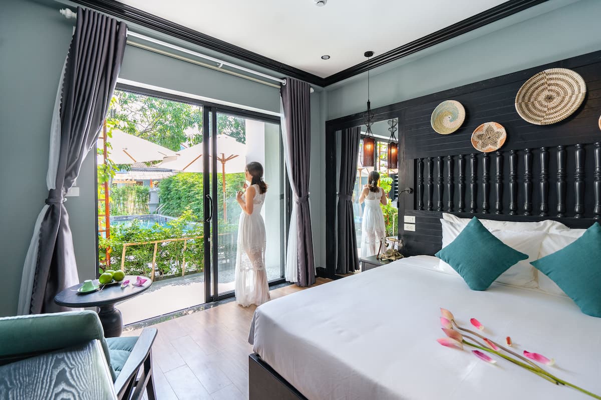 A hotel room with a large bed, a balcony with a view, and a dining area with a table and chairs.