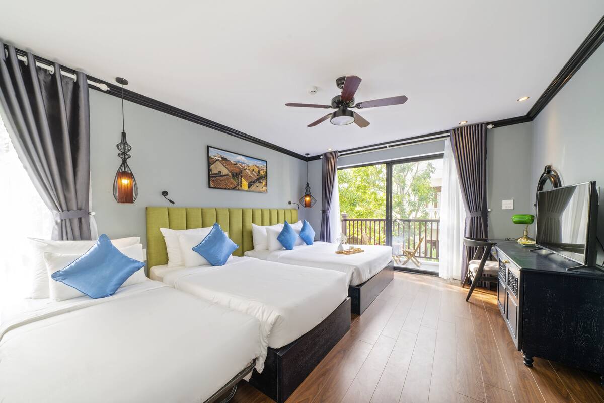A hotel room with two beds, a ceiling fan, a painting, and a balcony with a view.