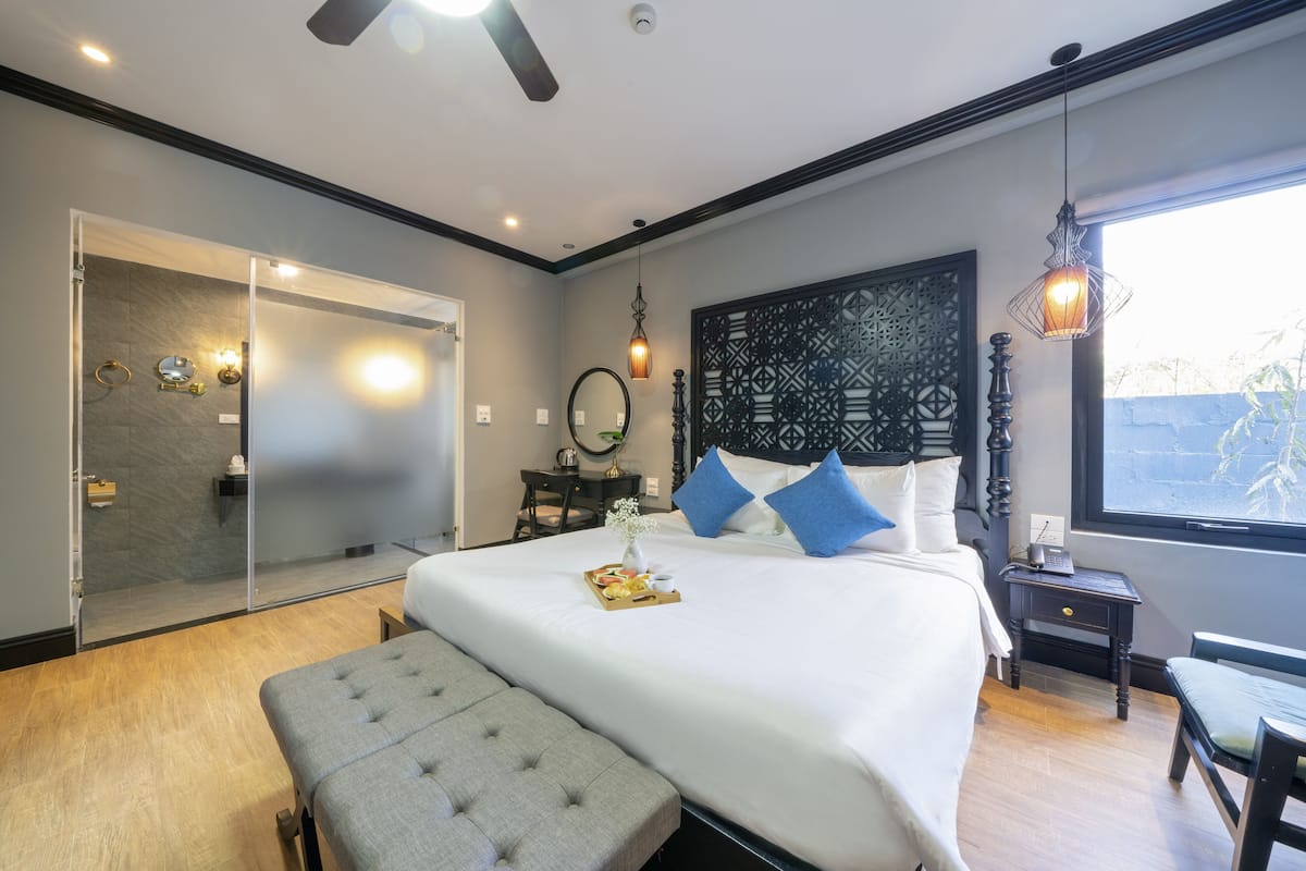 A modern hotel room with a large bed, a bench, a desk, and a view of the outdoors.