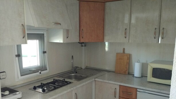 A compact kitchen with a gas stove, sink, and wooden cabinets. - Camping Iznate (Iznate)