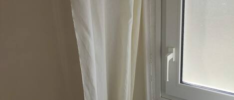 A bathroom with a toilet, a window, and a curtain.