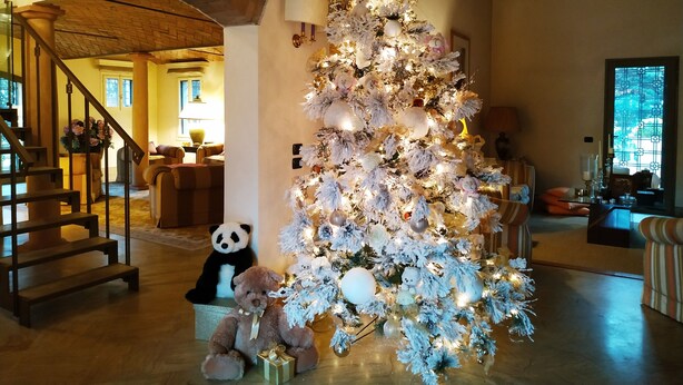 Uma árvore de Natal decorada numa sala de estar ampla, com escada e uma lareira acolhedora.