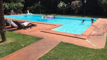 Une piscine dont les bords sont recouverts de carreaux, entourée d’une pelouse et agrémentée de plantes en pot.