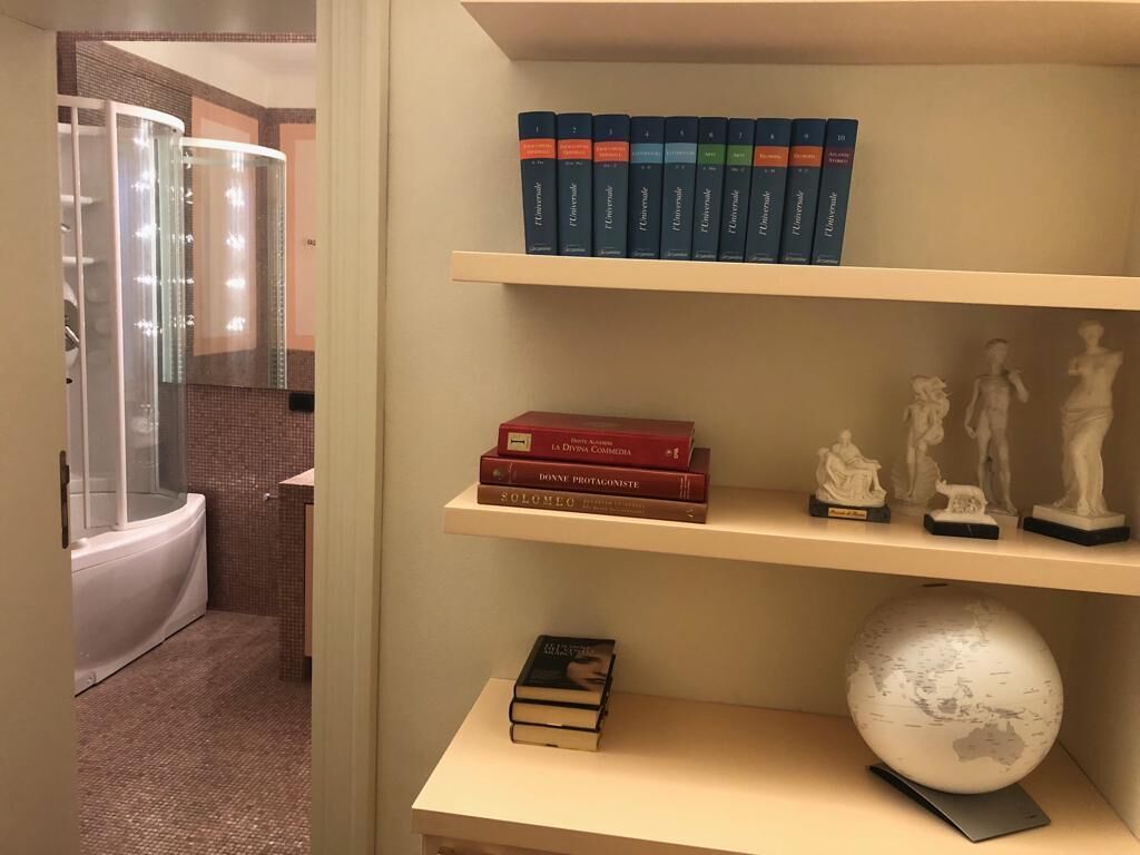 A bathroom with a glass shower enclosure, a sink, and a shelf with books and a globe.