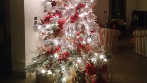 Árvore de Natal com enfeites e luzes vermelhas, rodeada por presentes embrulhados e um ursinho de pelúcia.