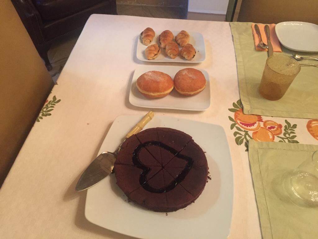 Una mesa con un pastel de chocolate, dos pequeñas rosquillas y un plato con dos bollos.