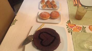 Una mesa con un pastel de chocolate, dos pequeñas rosquillas y un plato con dos bollos.