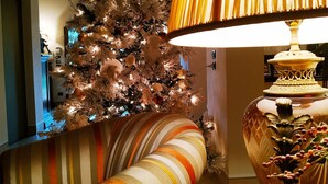 Uma sala de estar com um sofá listrado, uma árvore de Natal, um abajur e um relógio.