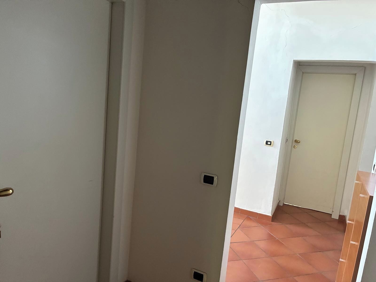 A corridor with a tiled floor, white walls, and a closed door at the end.
