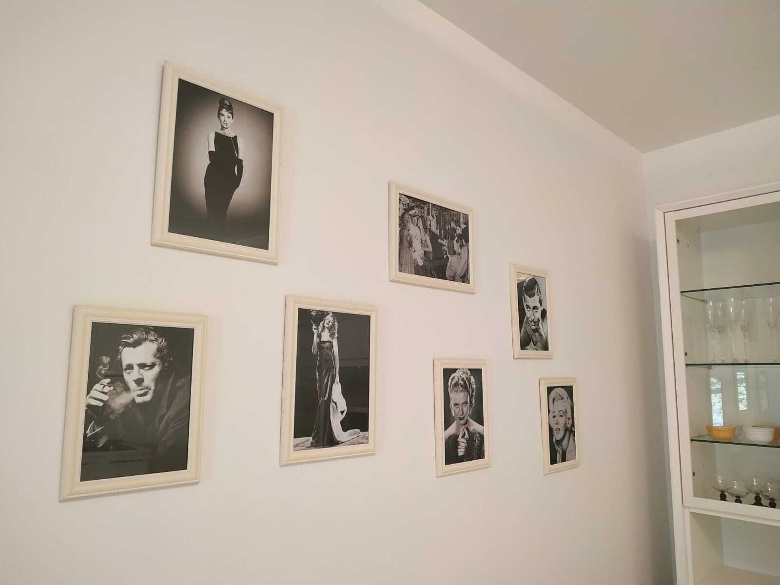 Una habitación con una pared blanca que exhibe seis fotografías blanco y negro enmarcadas. A la derecha, un aparador de vidrio con copas de vino.