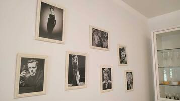Una habitación con una pared blanca que exhibe seis fotografías blanco y negro enmarcadas. A la derecha, un aparador de vidrio con copas de vino.