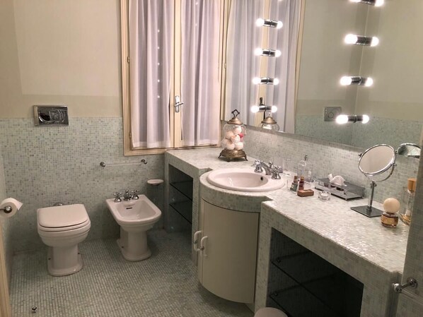 Un baño con inodoro, bidé, lavabo, tocador y espejo con iluminación.