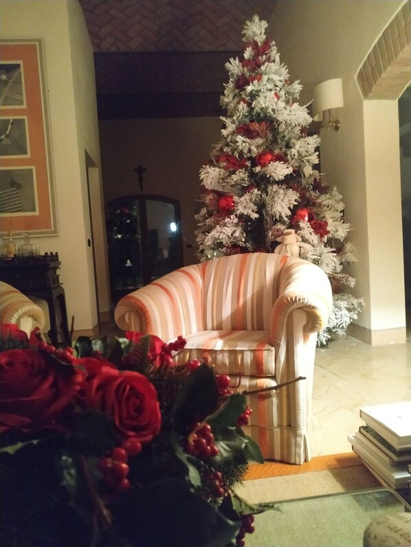 Una sala de estar con un sillón a rayas, un árbol de Navidad y un florero con rosas rojas.