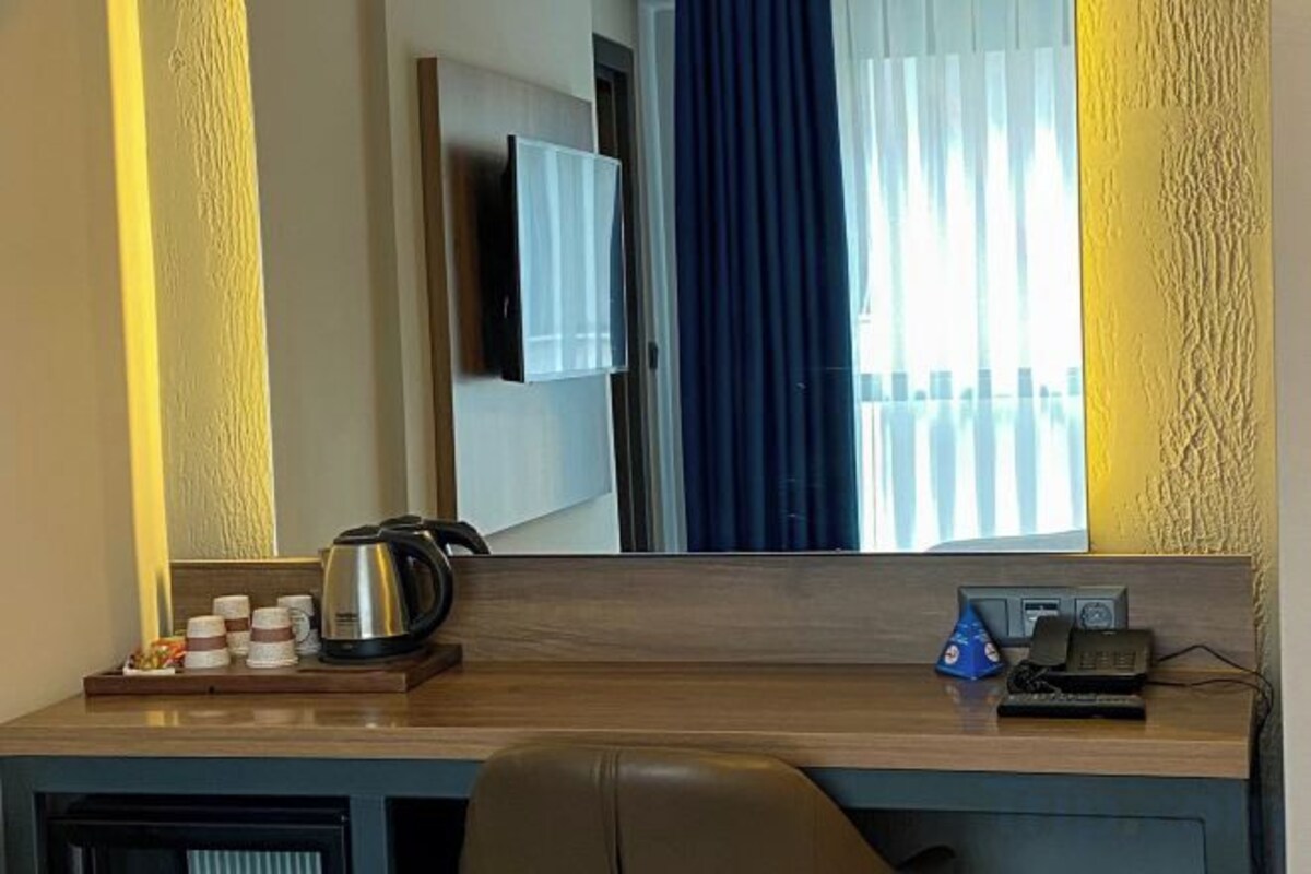 Una camera d'albergo con una scrivania in legno, una televisione a schermo piatto montata a parete, una finestra con tende e un letto con testiera.