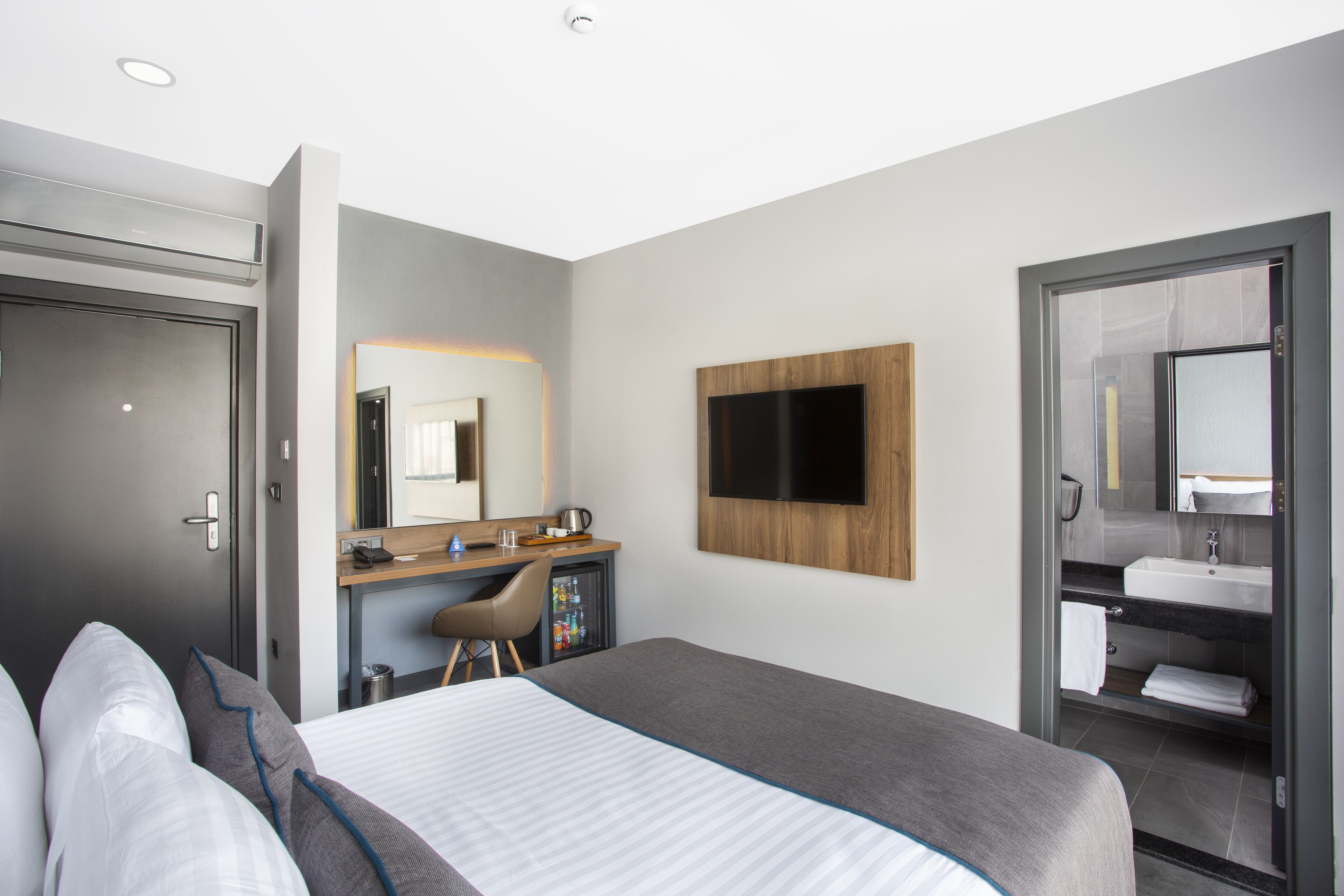 Habitación de hotel moderna con una cama, un escritorio, televisión y un baño visible a través de una puerta abierta.
