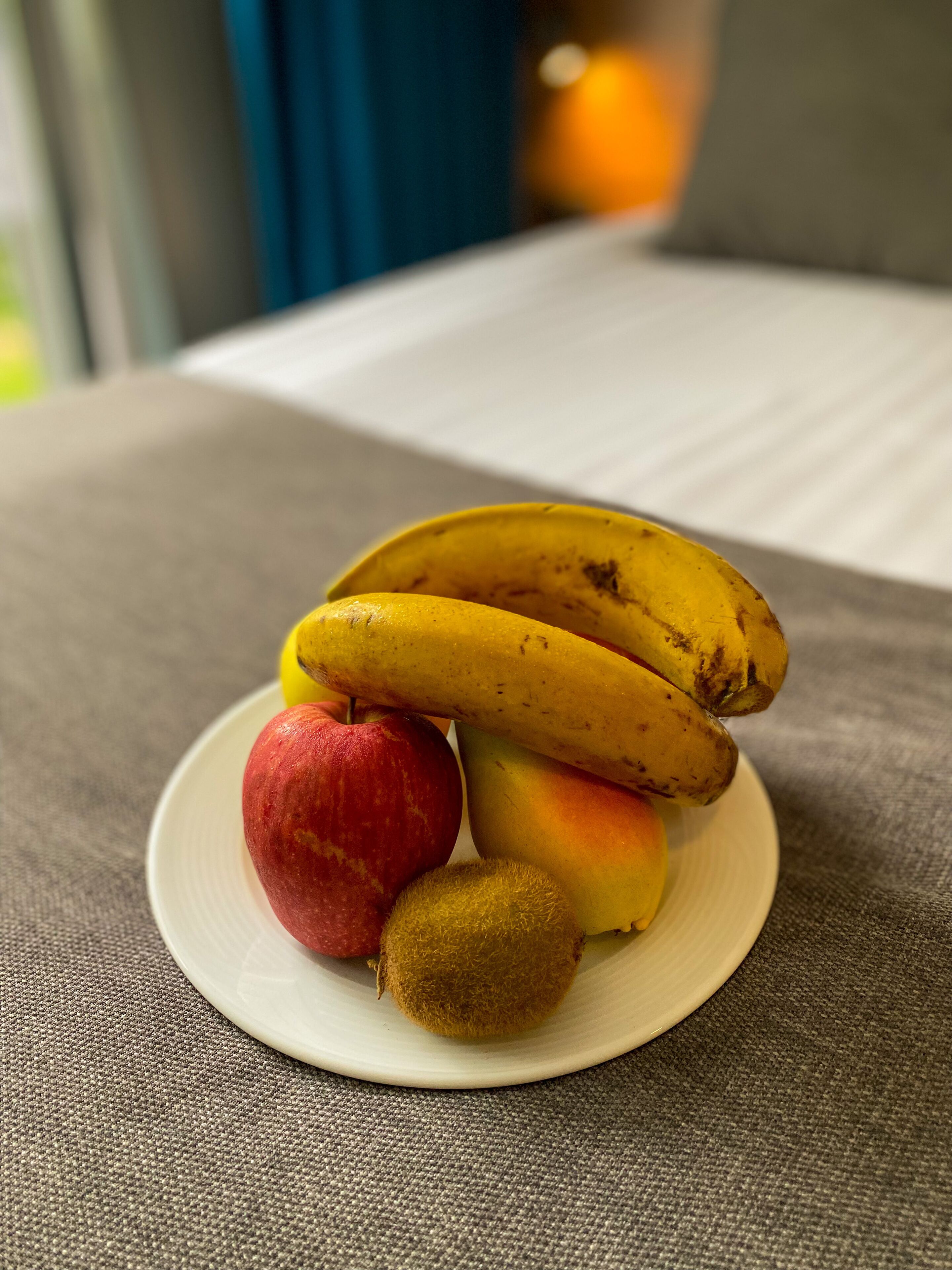 A plate with a banana, apple, peach, and kiwi on a textured surface.