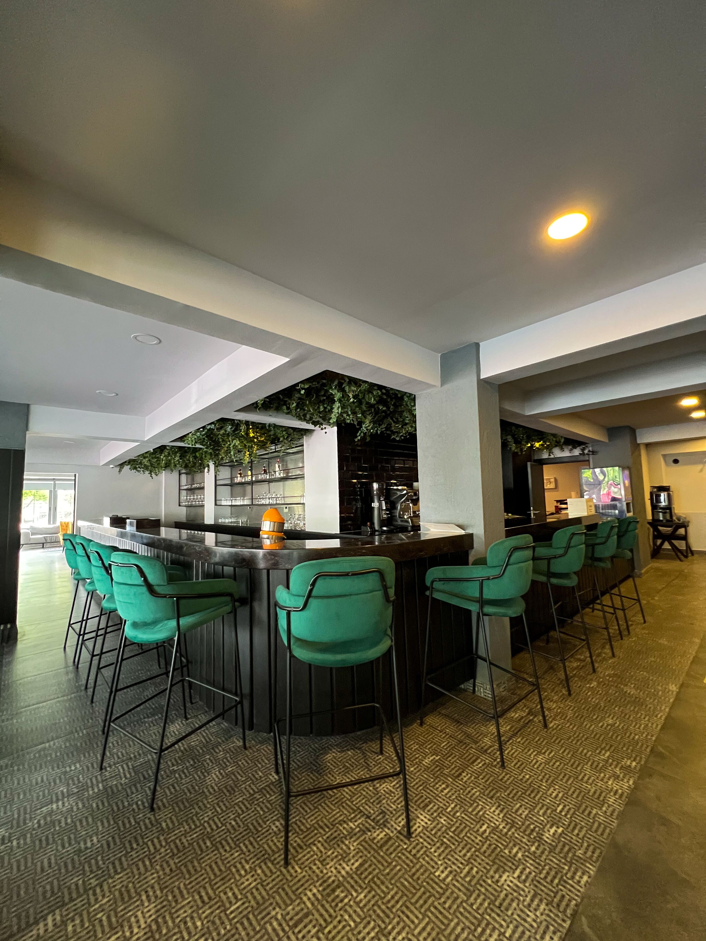 A modern bar area with green bar stools, a counter with a coffee machine, and a ceiling with a skylight.
