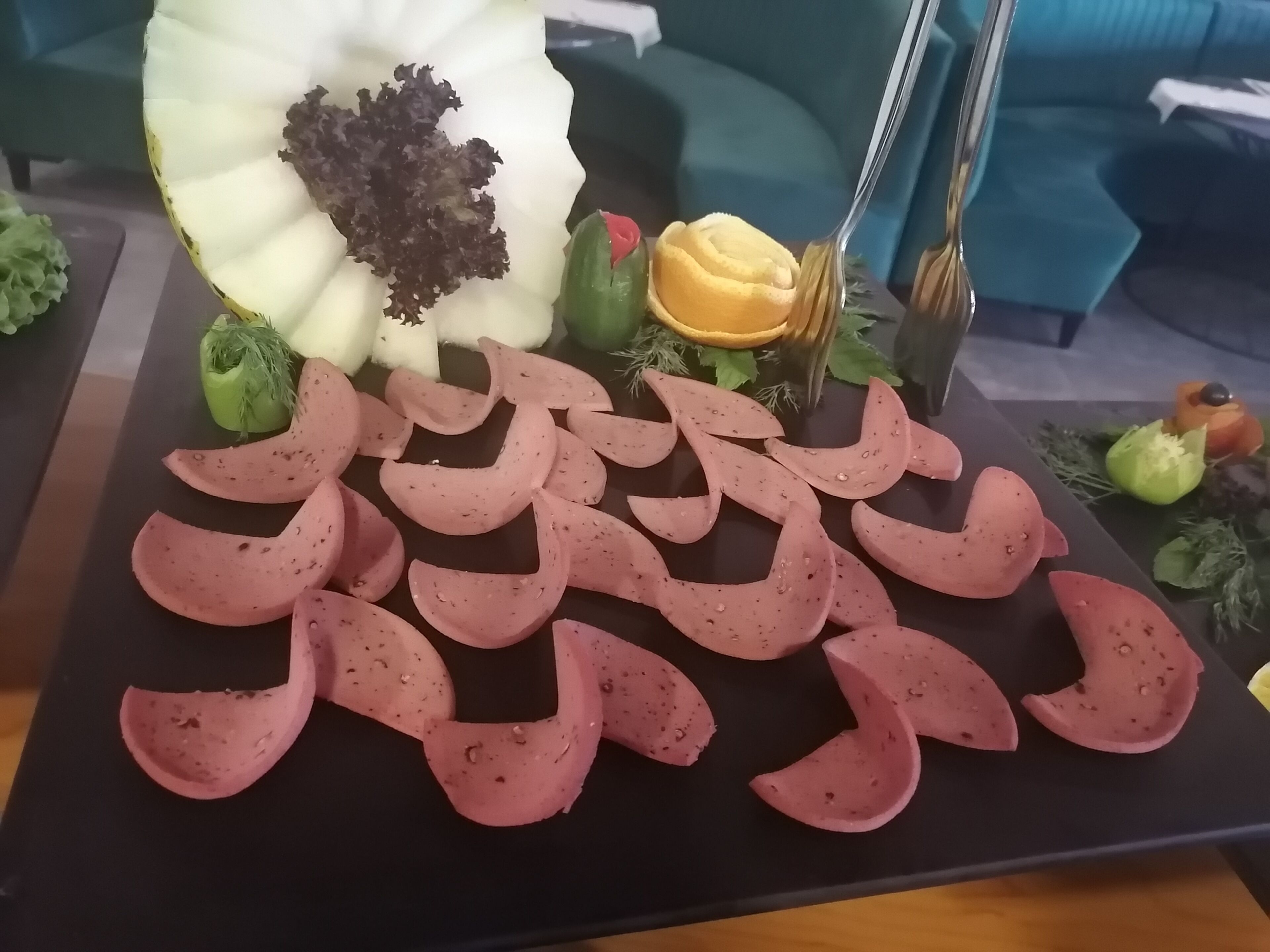 A platter with sliced meats and vegetables on a black tray.