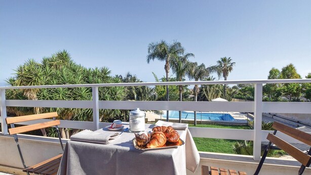 Un balcon avec une table préparée pour le petit-déjeuner, donnant sur une piscine et des palmiers.
