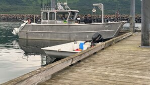 Ein an einem hölzernen Steg vertäutes Fischerboot mit Kabine und Außenbordmotor, vor dem Hintergrund grüner Hügel.