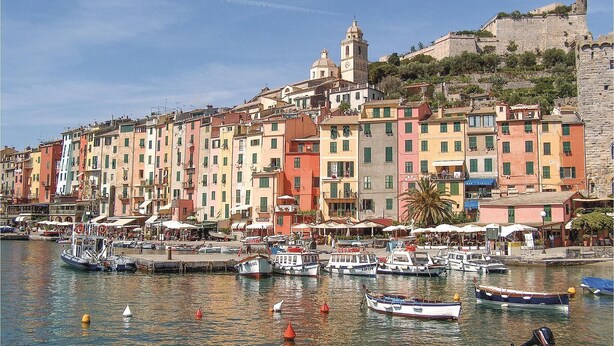 A waterfront with colorful buildings, a historic tower, and boats docked along the shore.