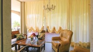 A room with a leather armchair, a wooden table with a vase of flowers, and a chandelier.