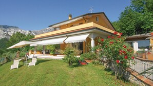 A two-story house with a balcony, a lawn, and a mountain backdrop.