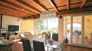 A spacious living area with a wooden ceiling, a glass dining table, and a television.